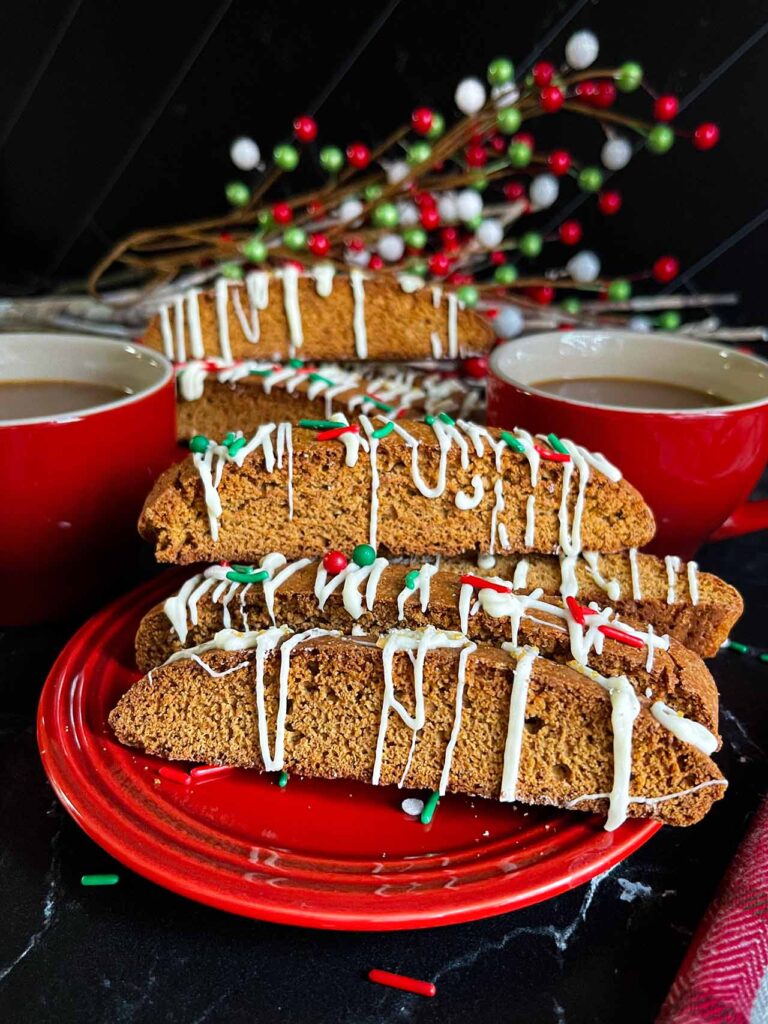Decorated gingerbread biscotti on small red plates with red coffee mugs.