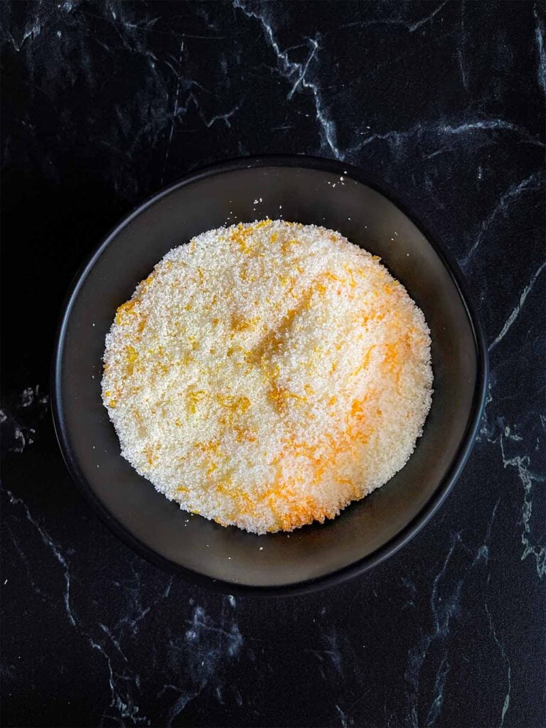 Tangerine zest mixed with the granulated sugar in a dark bowl.