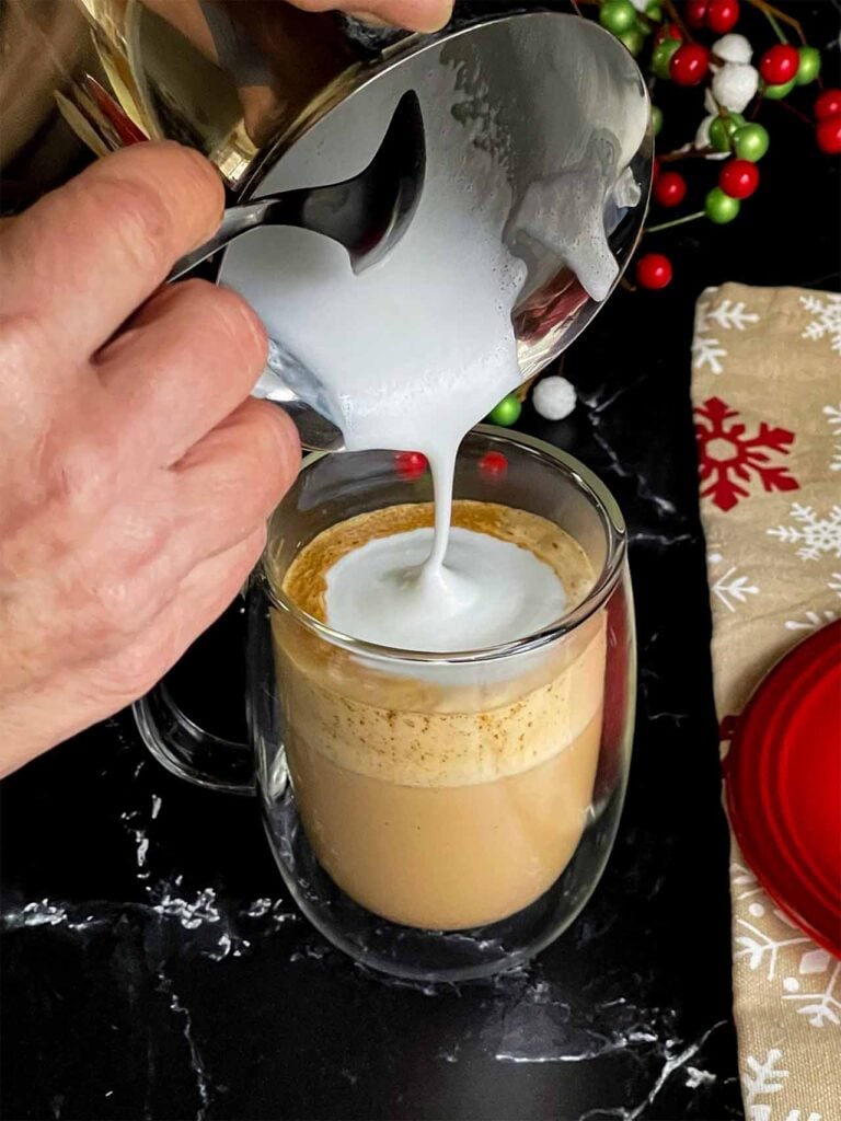 Steamed milk and foam being poured into the glass mug.