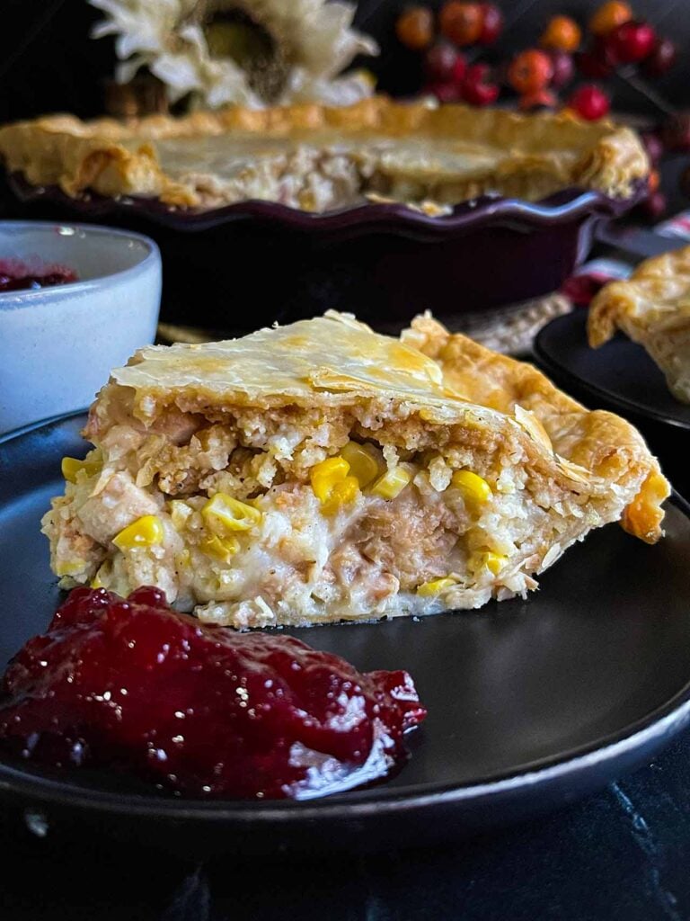 A slice of leftover thanksgiving pie on a black plate with cranberry sauce on the side.