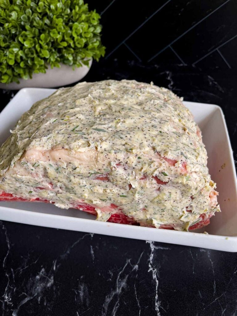 Prime rib coated in a butter compound placed in a shallow roasting pan.