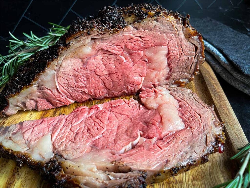 Slice prime rib on a cutting board garnished with fresh rosemary.