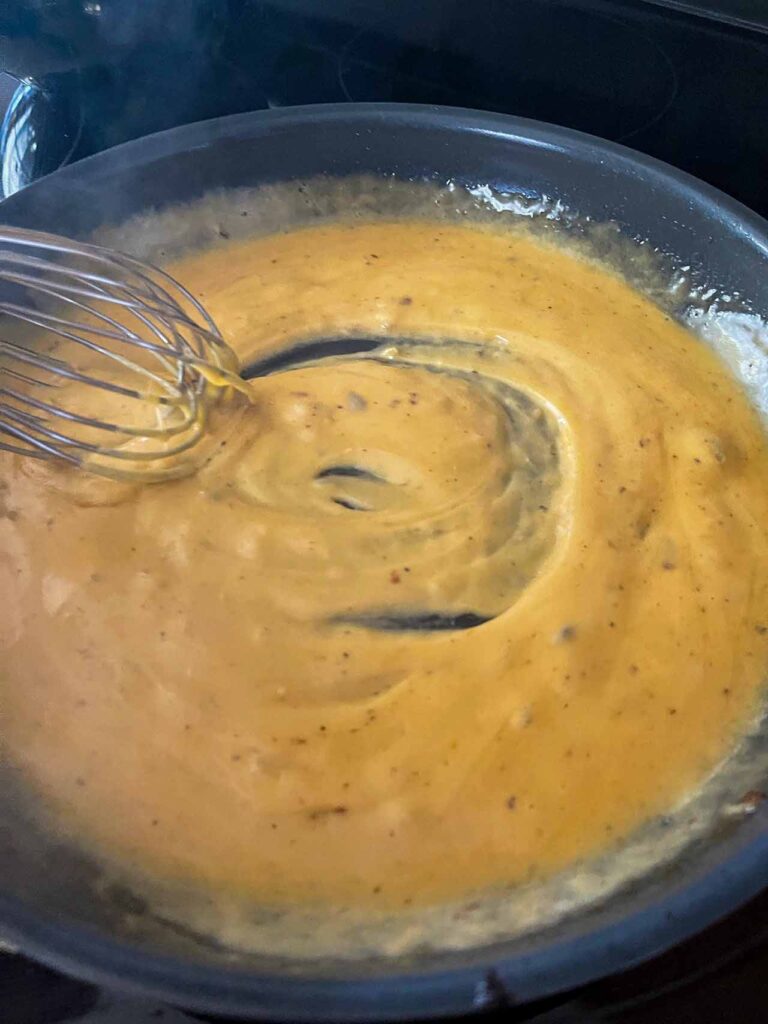 A cheese sauce in a skillet being whisked.