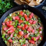 Queso fundido in a cast iron skillet with tortillas in a black bowl.