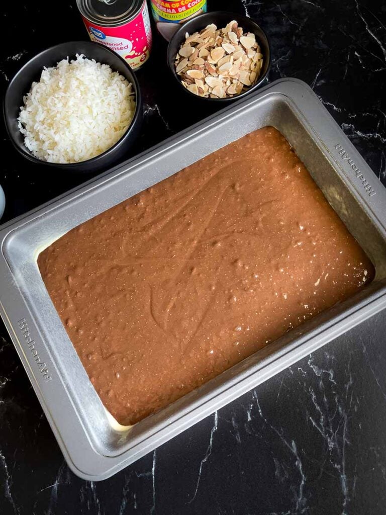 Almond Joy cake batter poured into a 9x13 pan with the coconut, almonds, and chocolate chips behind the pan.