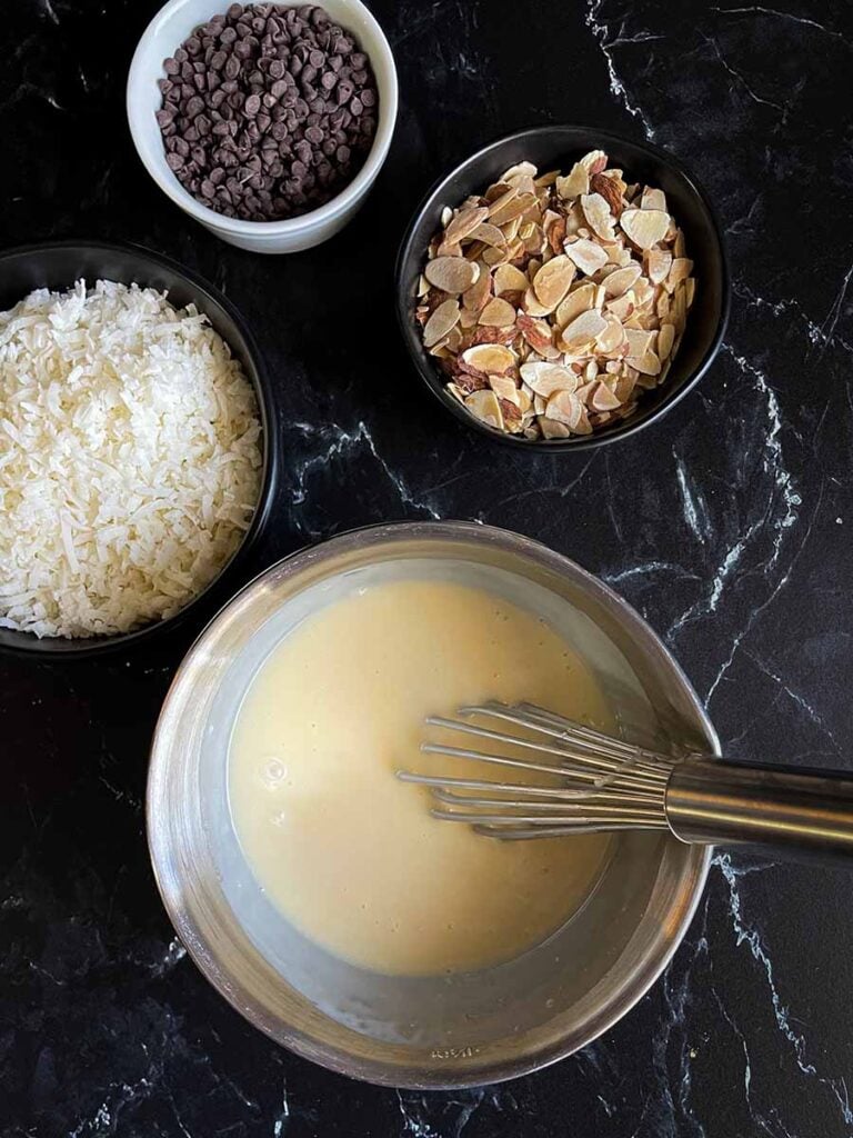 Sweetened condensed milk mixed with cream of coconut in a metal bowl.