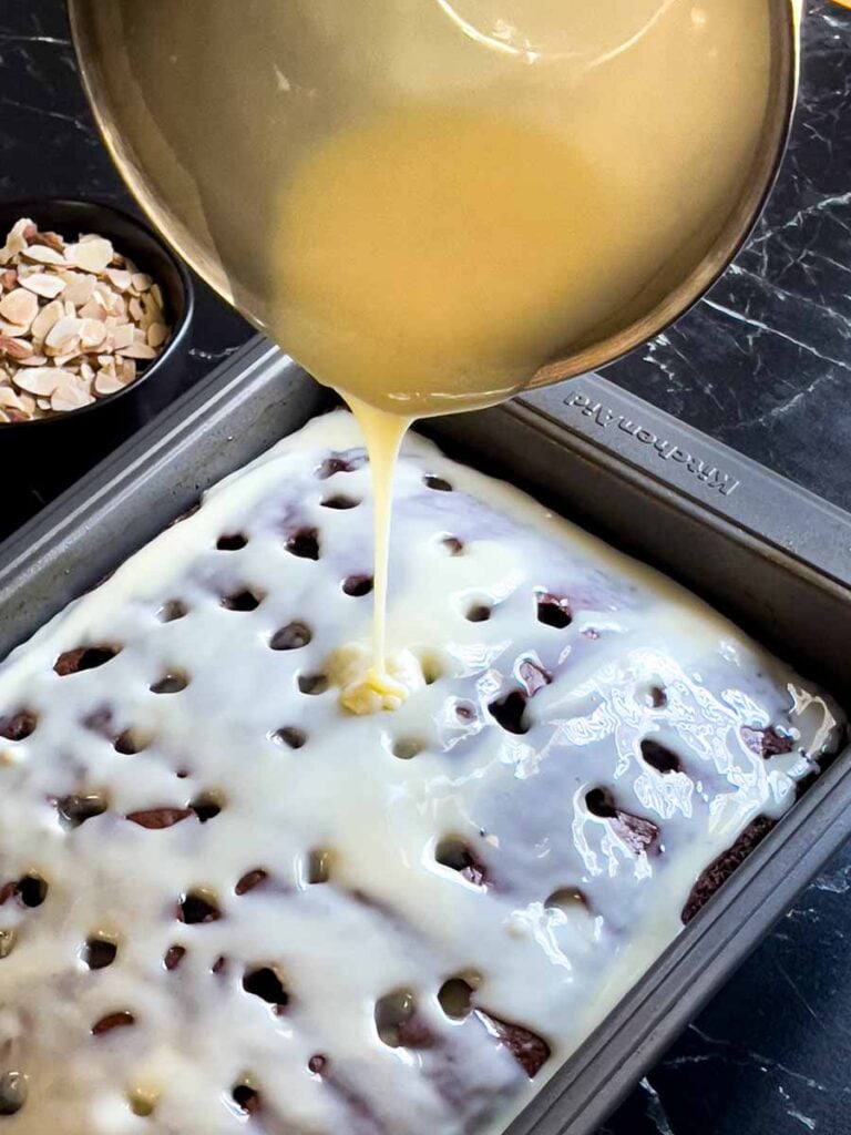 The milk mixture being poured over the Almond Joy cake with holes poked into it.