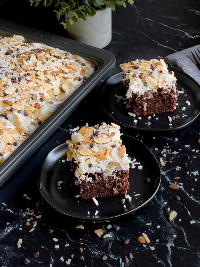 Slices of Almond Joy cake on dark plates with the cake pan next to them.