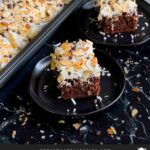 Almond Joy Cake is a rich and decadent chocolate cake, soaked with coconut cream sauce, and topped with sweet coconut, whipped cream topping, almonds, and semi-sweet chocolate chips.