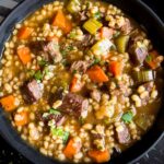 Beef barley soup in a dark bowl garnished with chopped parsley.