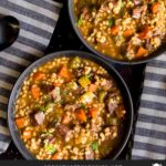 Beef barley soup in a dark bowl.