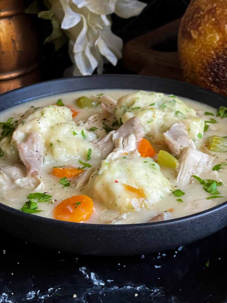 Homemade chicken and dumplings in a dark bowl.