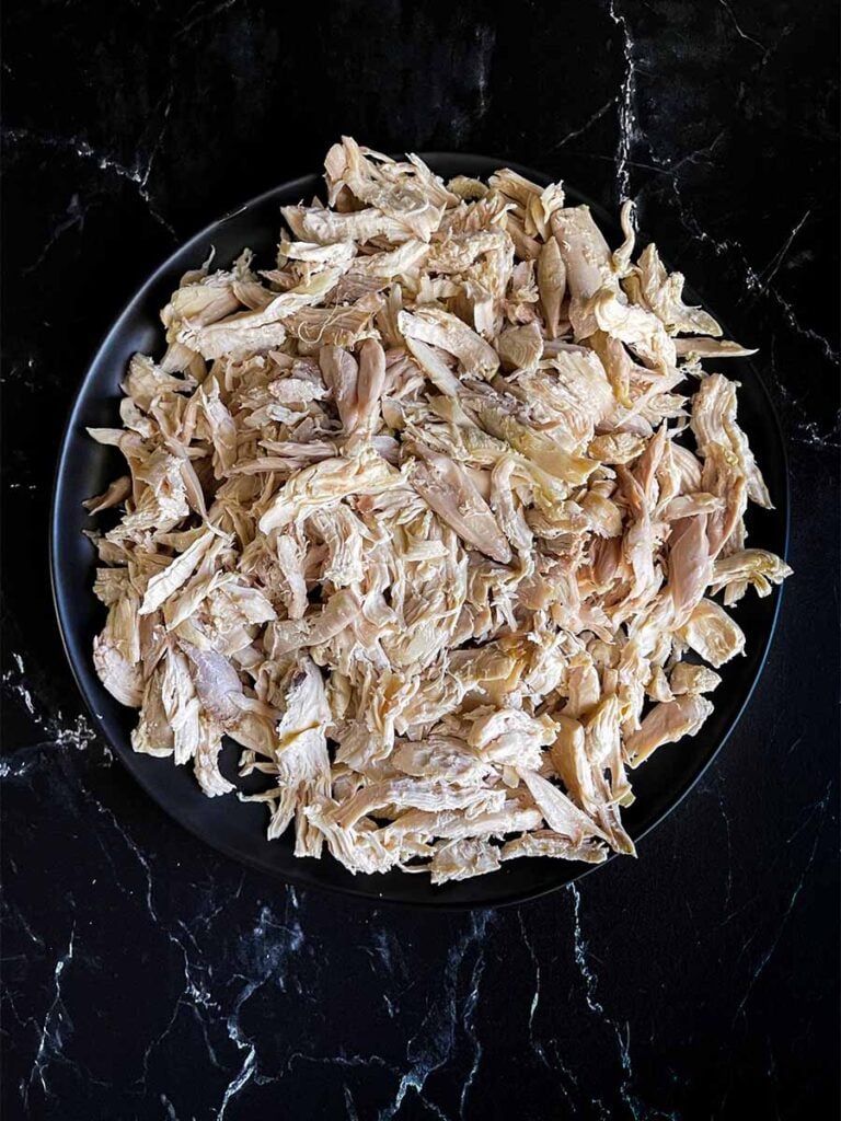 Cooked, shredded chicken on a dark plate.