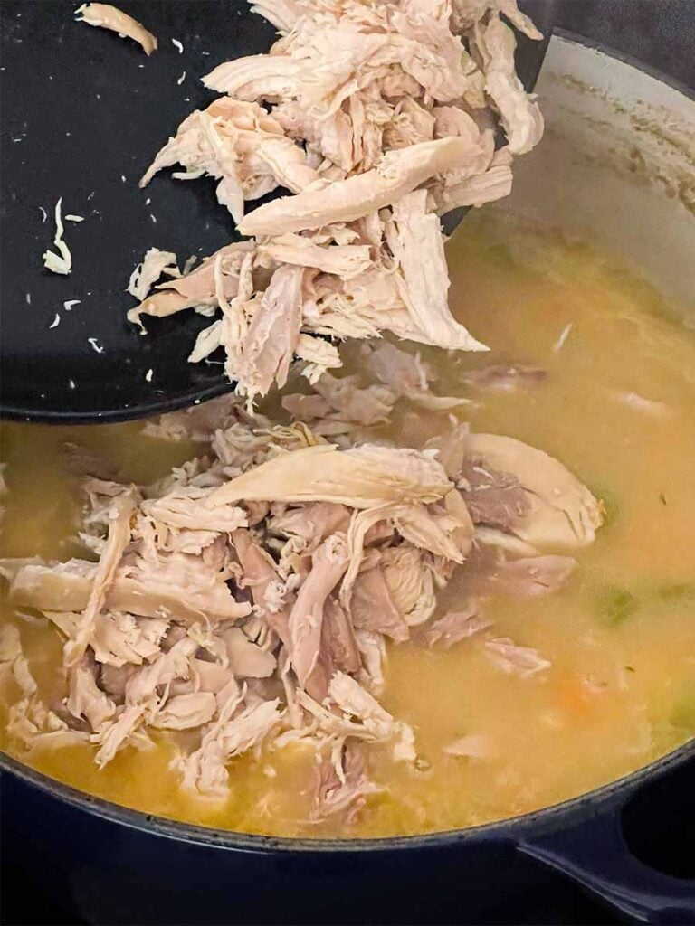 Adding cooked chicken to the chicken soup.