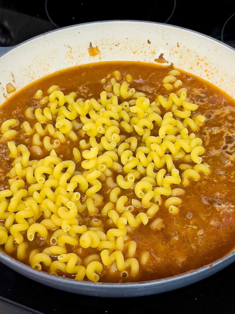 Uncooked pasta just added to beef stock in a cast iron skillet.