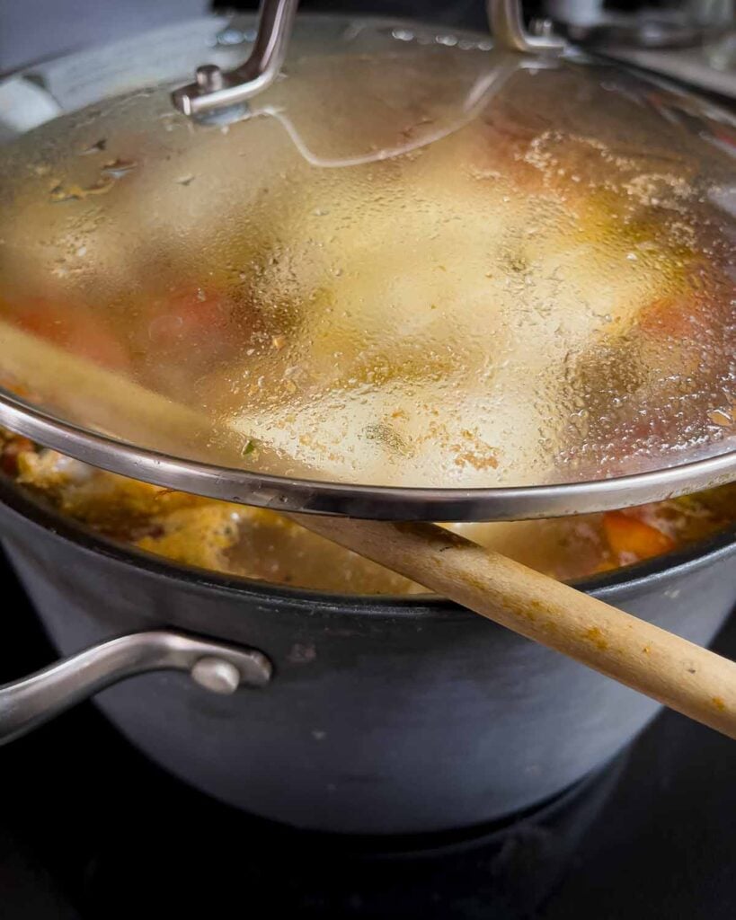 Sicilian chicken noodle soup simmering with the lid propped slightly open using a wooden spoon.