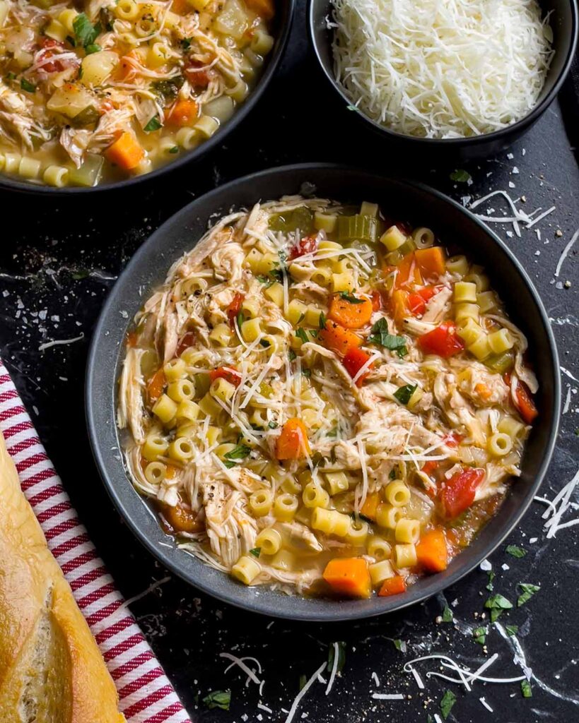 Sicilian chicken noodle soup in a dark bowl garnished with fresh parsley and Pecorino Romano cheese.