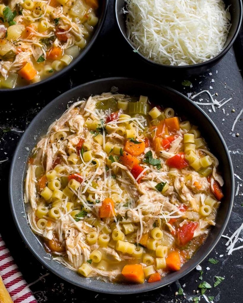 Sicilian chicken noodle soup in a dark bowl garnished with fresh parsley and Pecorino Romano cheese.