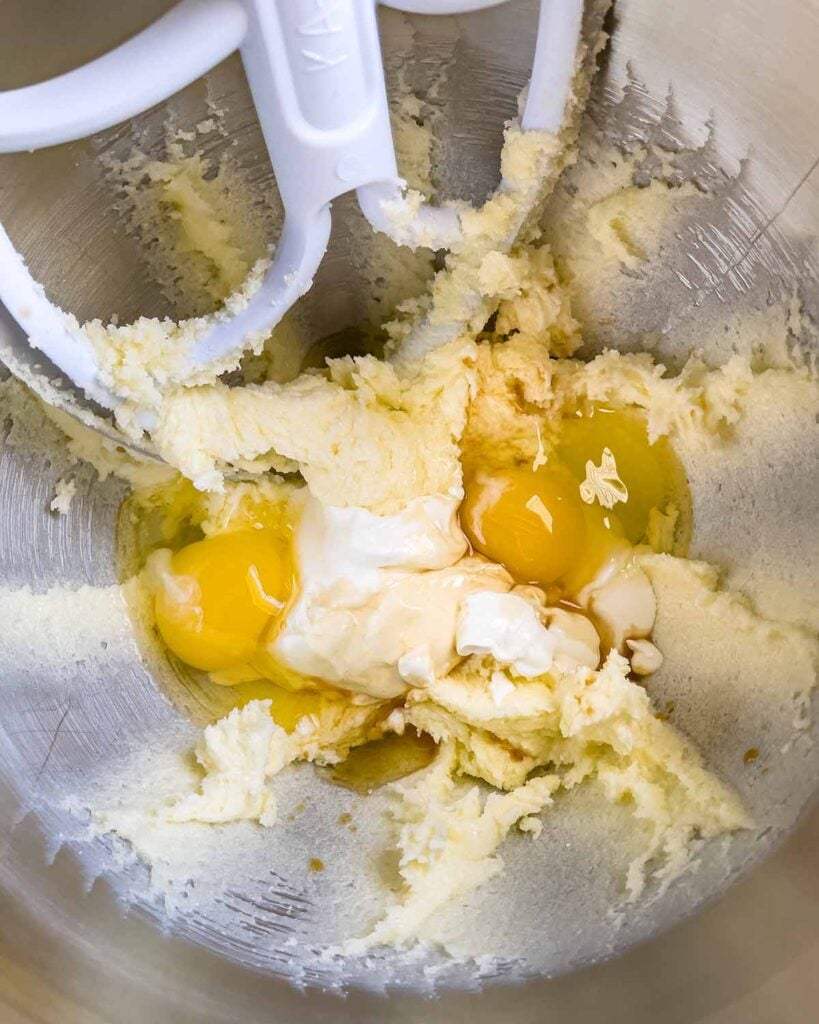 Eggs, sour cream, and vanilla extract added to the creamed butter in a metal mixing bowl.