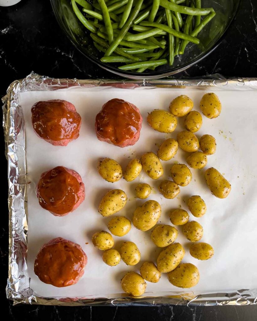 Potatoes added to the sheet pan with the mini meatloaves with the green beans in the background.