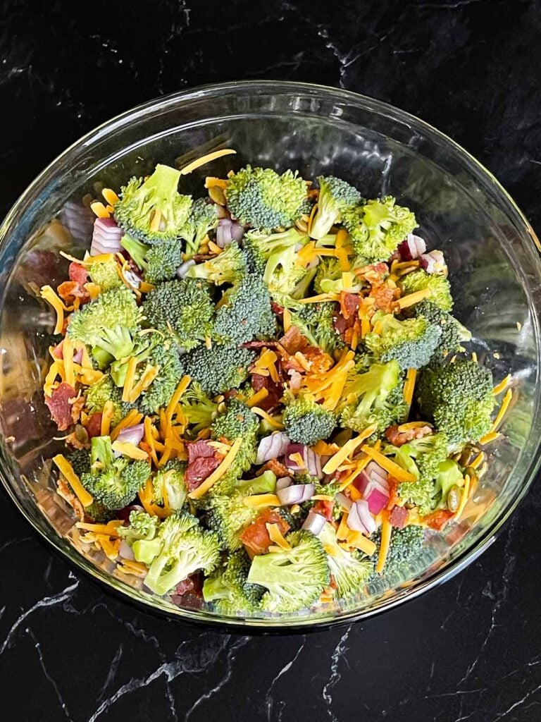 Broccoli salad ingredients tossed in a large glass mixing bowl.