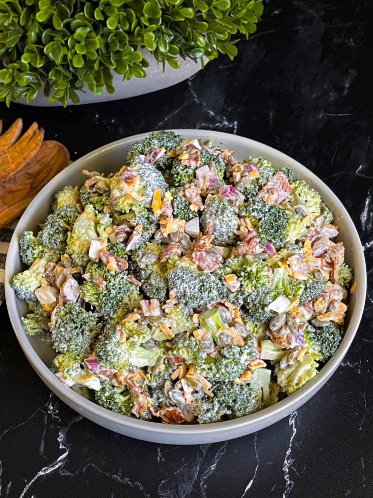 Broccoli salad in a light bowl with a plant in the background.