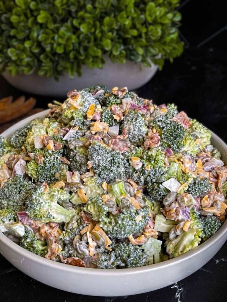 Broccoli salad in a light bowl with a plant in the background.