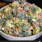 Broccoli salad in a light bowl with a plant in the background.