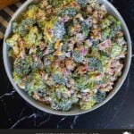 Broccoli salad in a light bowl with a plant in the background.