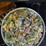 Broccoli salad in a light bowl with a plant in the background.