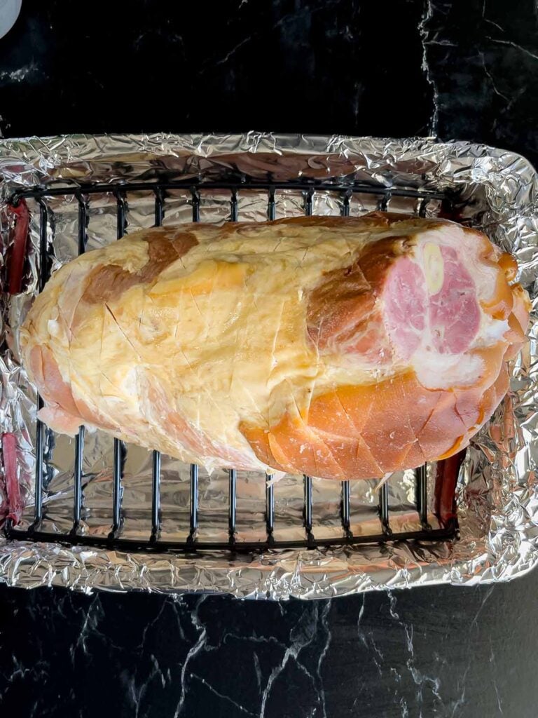 Prepared ham placed on a rack inside a foil lined roasting pan on top of a rack inside a foil lined roasting pan.