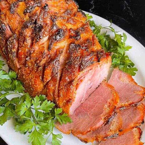 Brown sugar glazed ham on a platter garnished with fresh parsley.