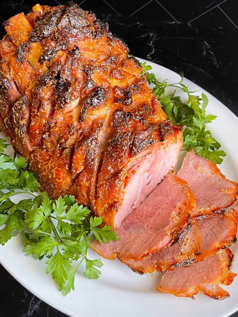 Brown sugar glazed ham on a platter garnished with fresh parsley.