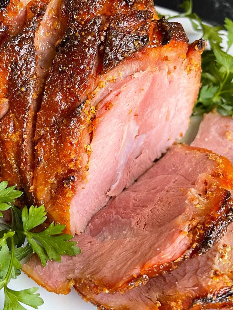 Brown sugar glazed ham on a platter garnished with fresh parsley.