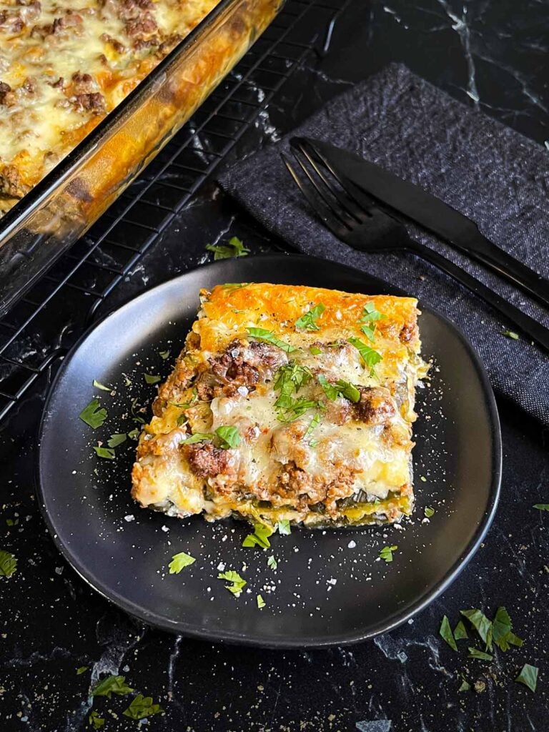 A serving of chile relleno casserole on a dark plate with the casserole in the background.