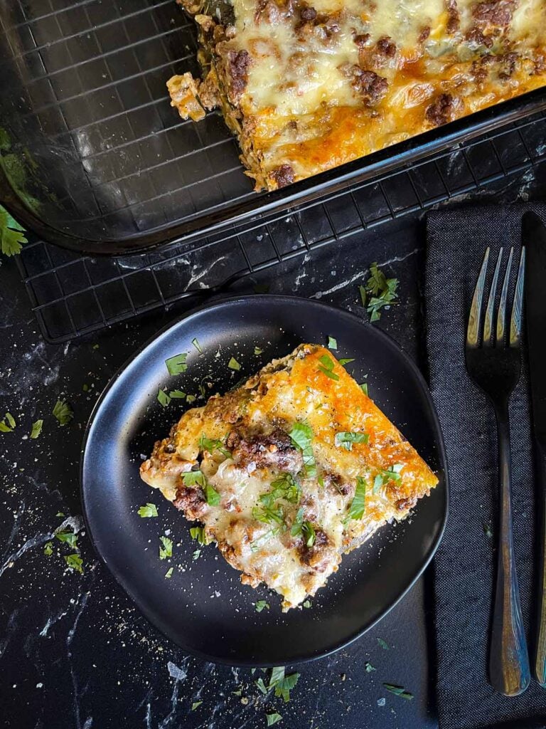 A serving of chile relleno casserole on a dark plate with the casserole in the background.