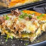 A serving of chile relleno casserole on a dark plate with the casserole in the background.