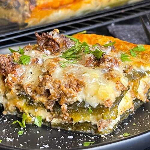 A serving of chile relleno casserole on a dark plate with the casserole in the background.