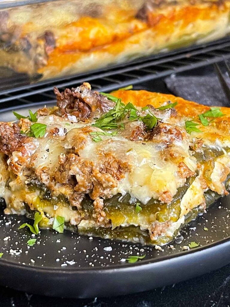 A serving of chile relleno casserole on a dark plate with the casserole in the background.