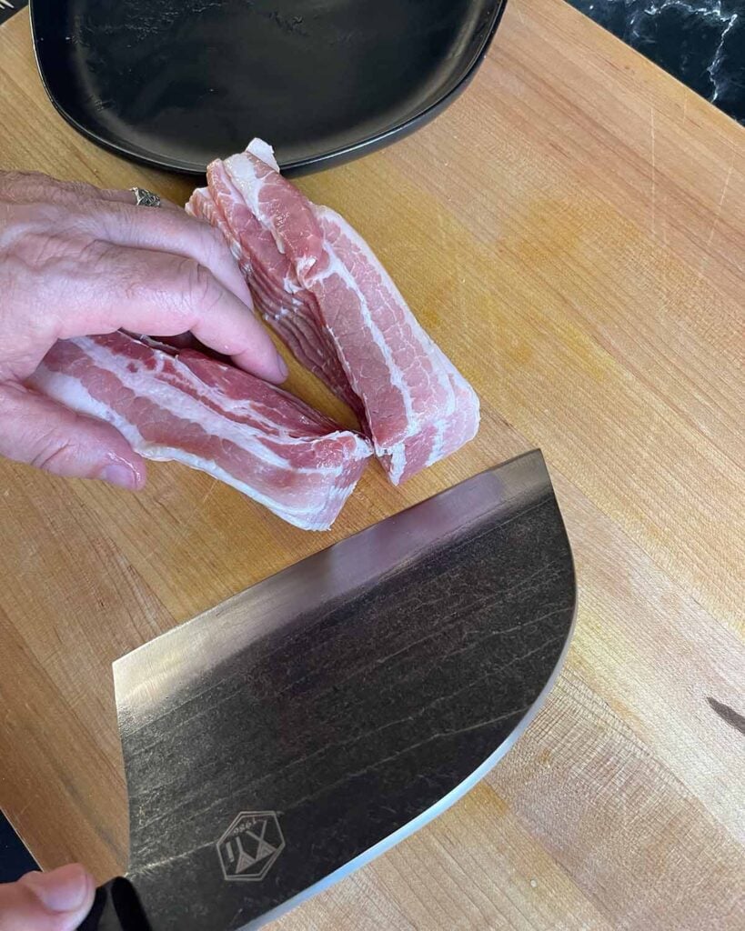 Cutting bacon in half on a cutting board.