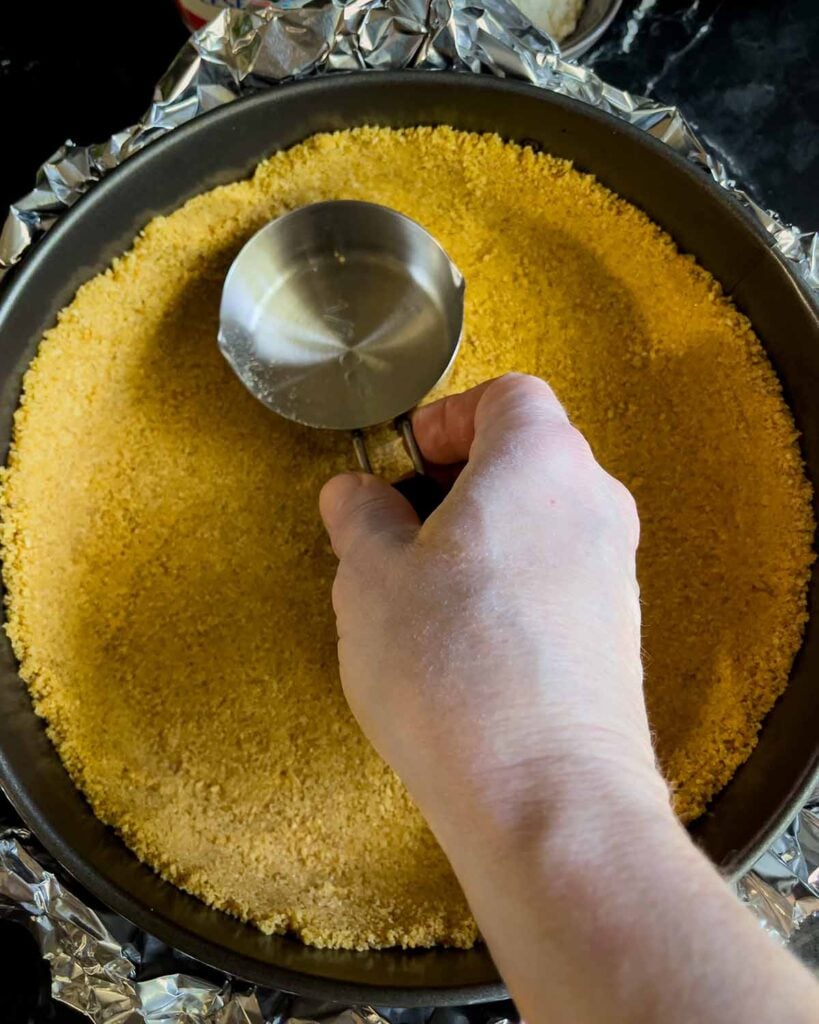 Graham cracker crust pressed into the springform pan using a metal measuring cup.