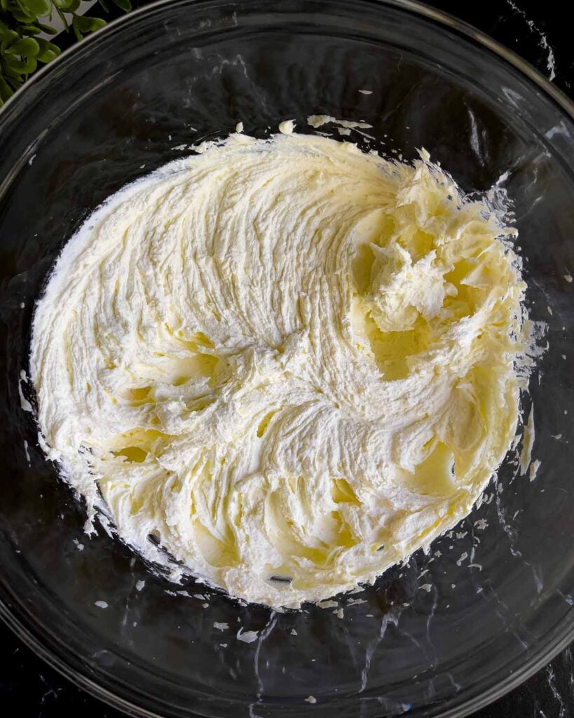 Ricotta cheese and mascarpone cheese beat together in a glass mixing bowl.