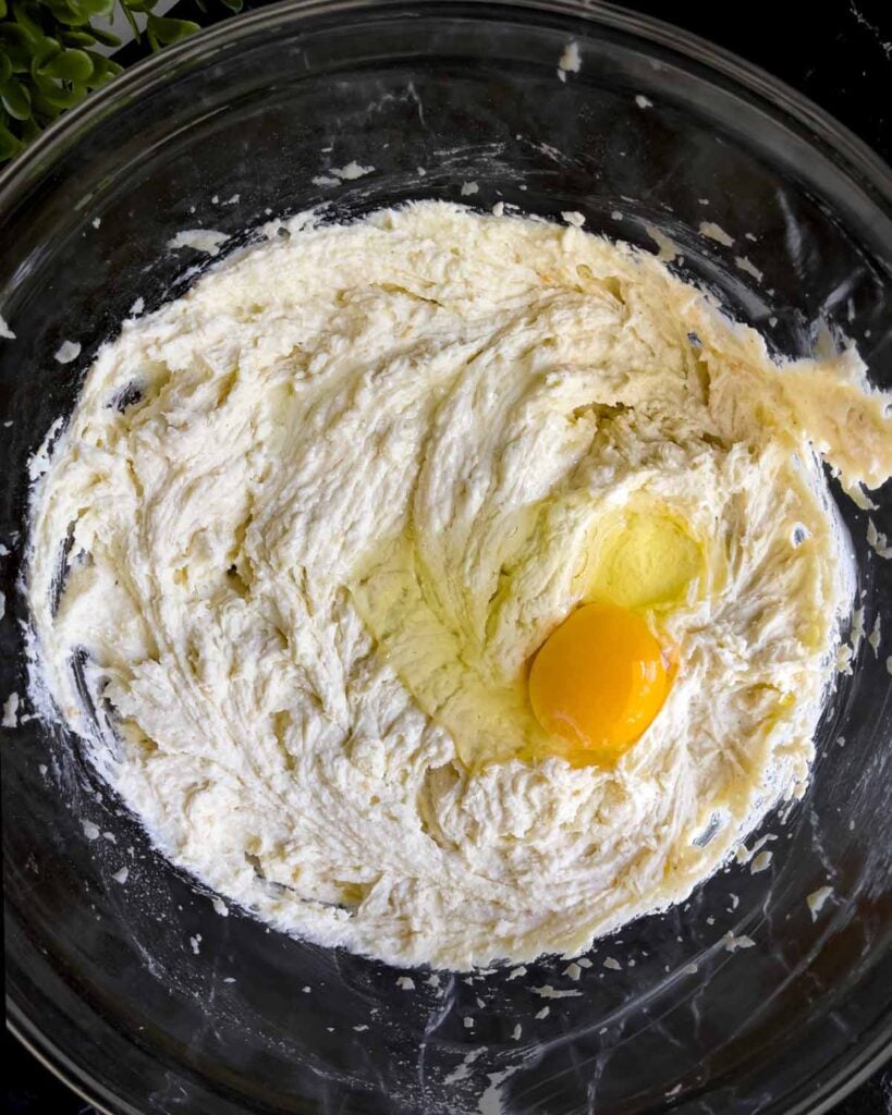 Eggs being added to the cannoli cheesecake mixture in a glass bowl.