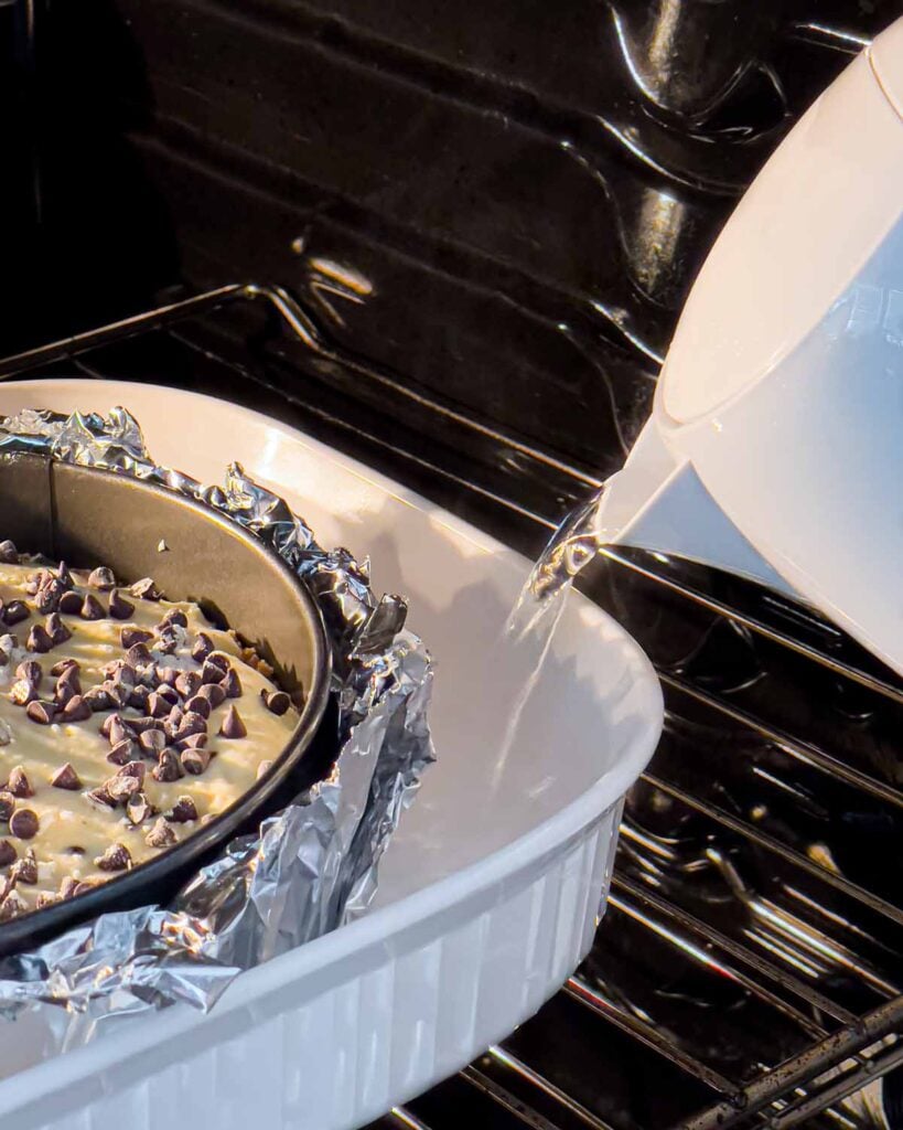 The cannoli cheesecake in the oven adding the boiling water to the roasting pan.