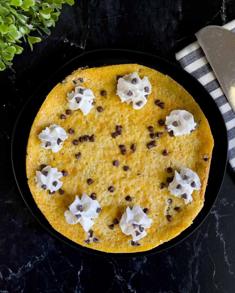 The whole cannoli cheesecake garnished with whipped cream and chocolate chips on a dark plate.