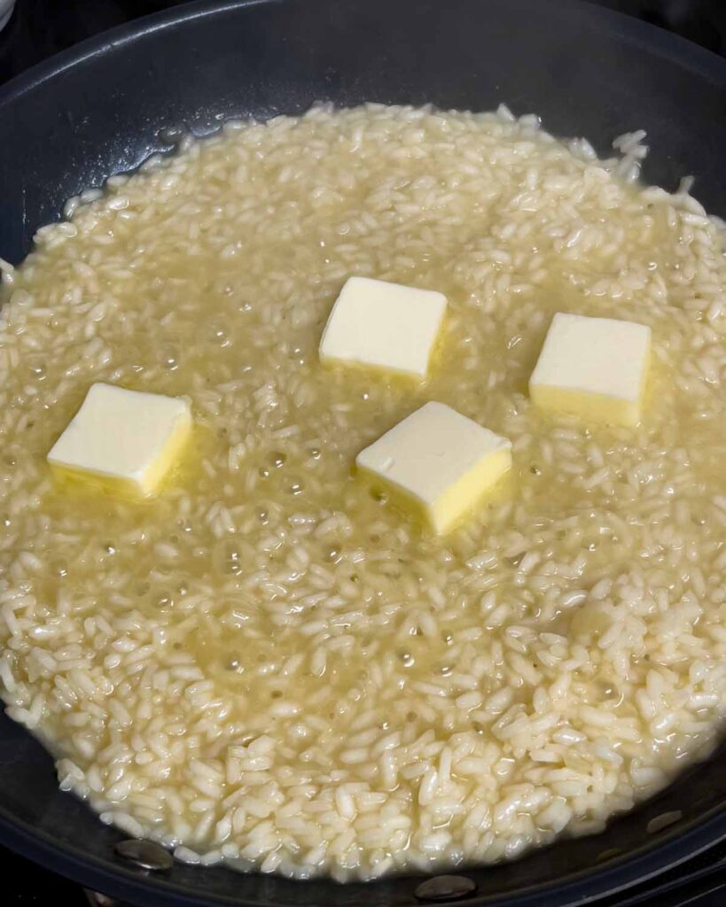 Adding butter to risotto in a skillet.