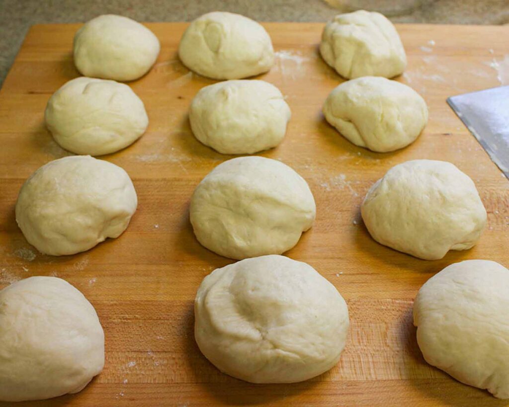 Naan dough balls formed on a wooden board.