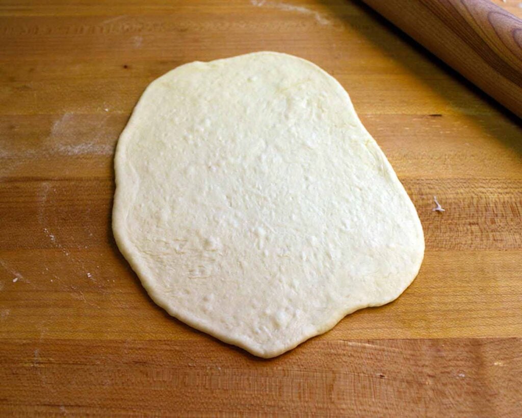 Naan dough ball rolled out into a circle on a wooden board.