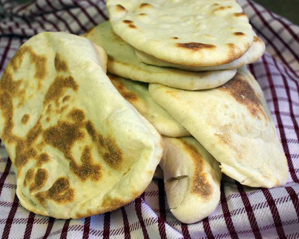 Homemade naan flatbread stacked on a red and white kitchen towel.