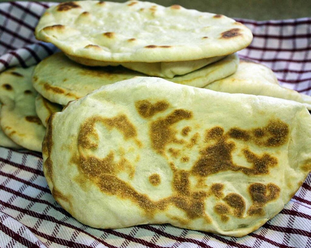Homemade naan flatbread stacked on a red and white kitchen towel.